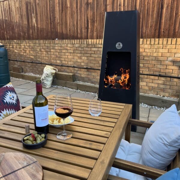 Luxury Metal Chiminea with fire lit in front of table with wine and snacks Square